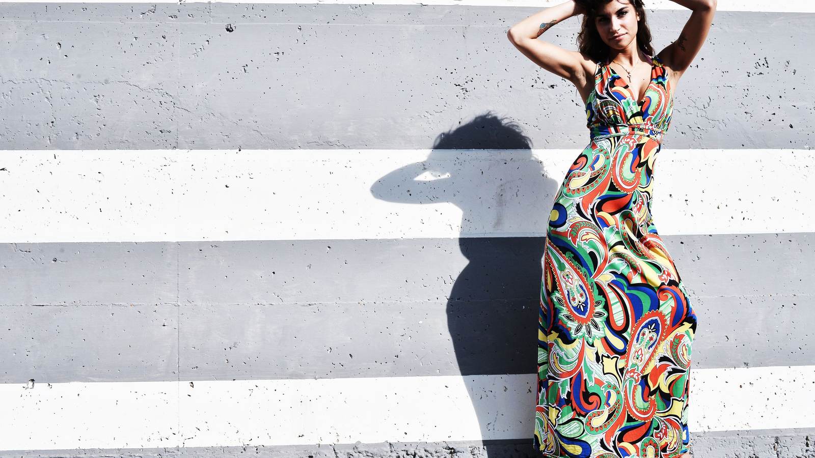 Femme en robe longue à motifs colorés devant un mur rayé noir et blanc