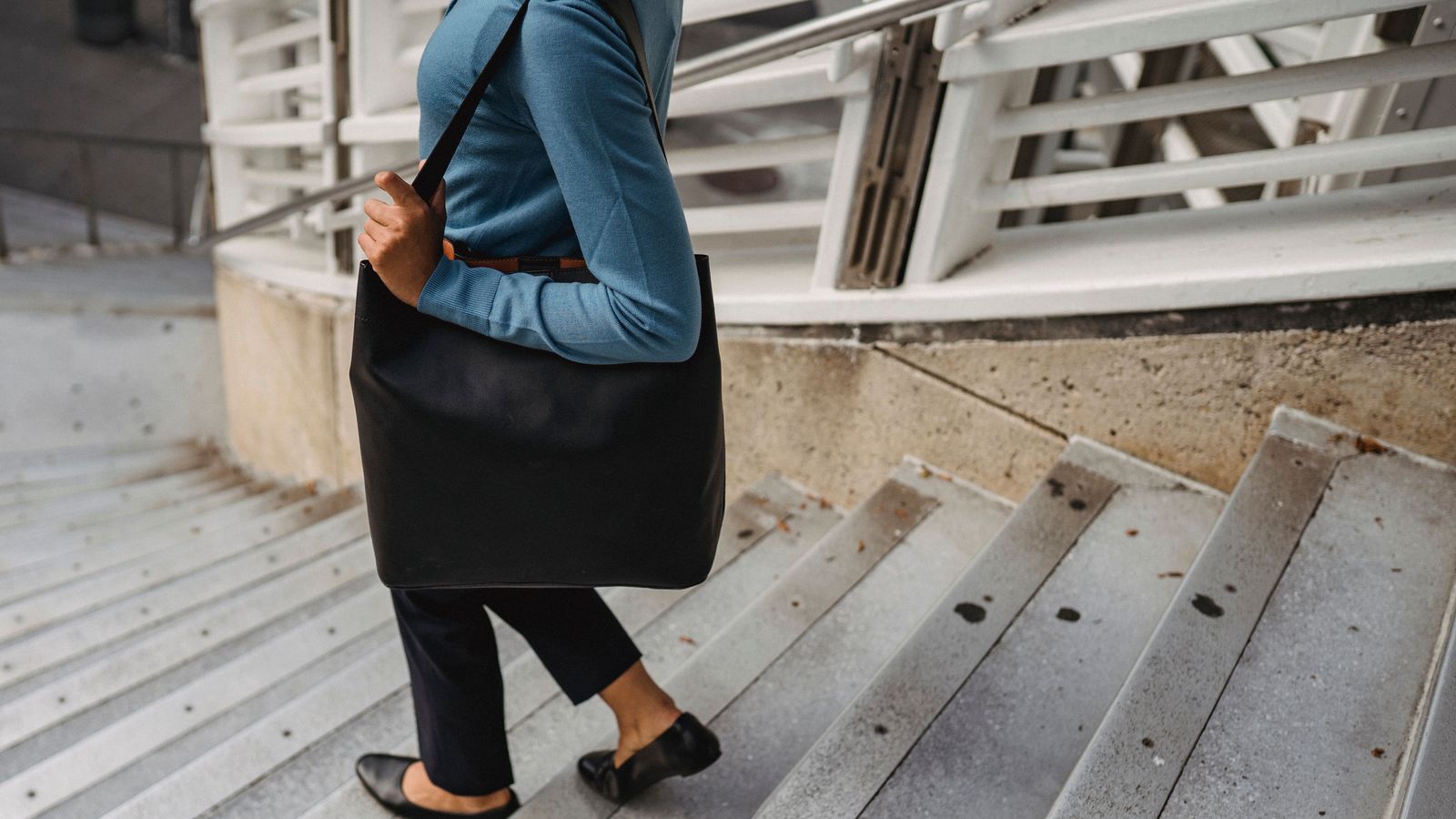 02 sactravail Femme descendant des escaliers avec un cabas noir porté à l'épaule