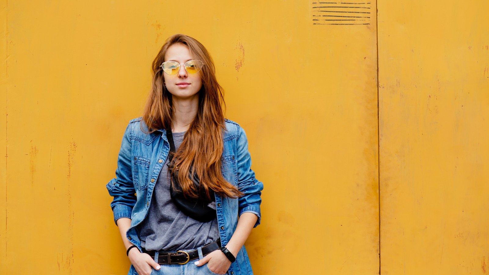 04 denim Femme en chemise et jean en denim devant un mur jaune