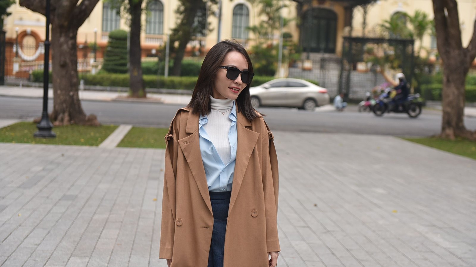 06 t2818 Femme en manteau camel porté sur une chemise bleu clair et un jean, dans la rue