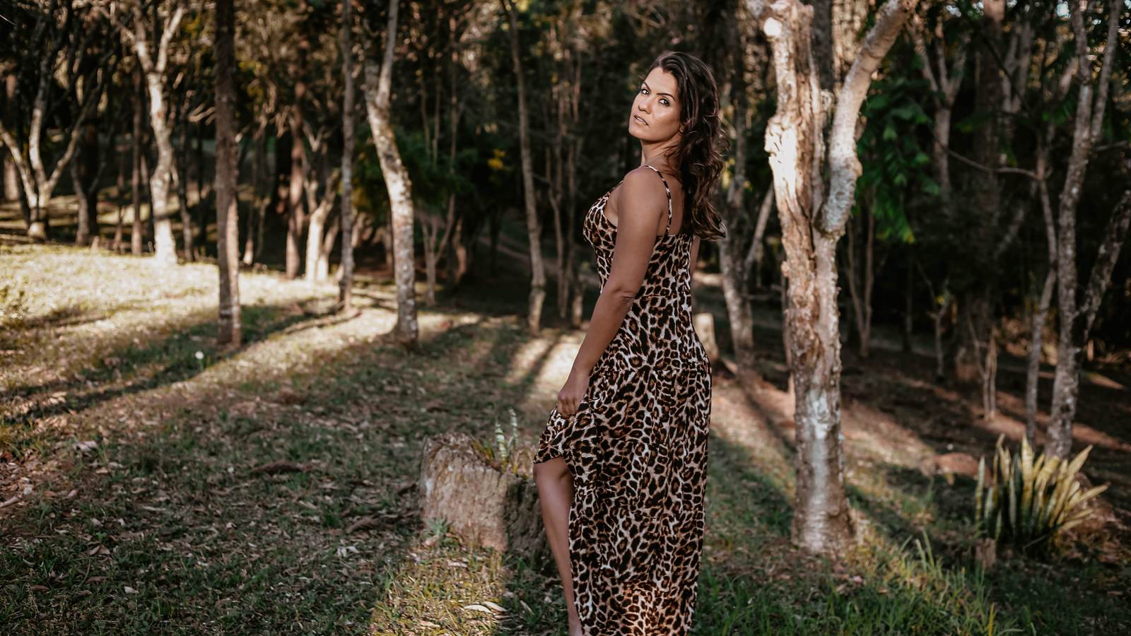 Femme en robe longue à motif léopard dans un bois éclairé par le soleil