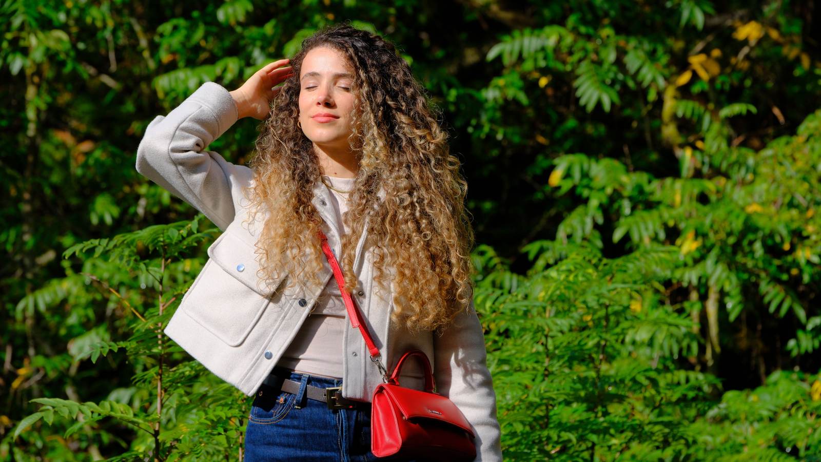 09 sacrouge Sac rouge porté en bandoulière sur une veste claire, en extérieur