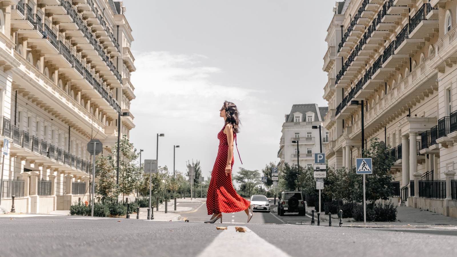 Femme en robe longue rouge marchant au milieu d'une rue haussmannienne